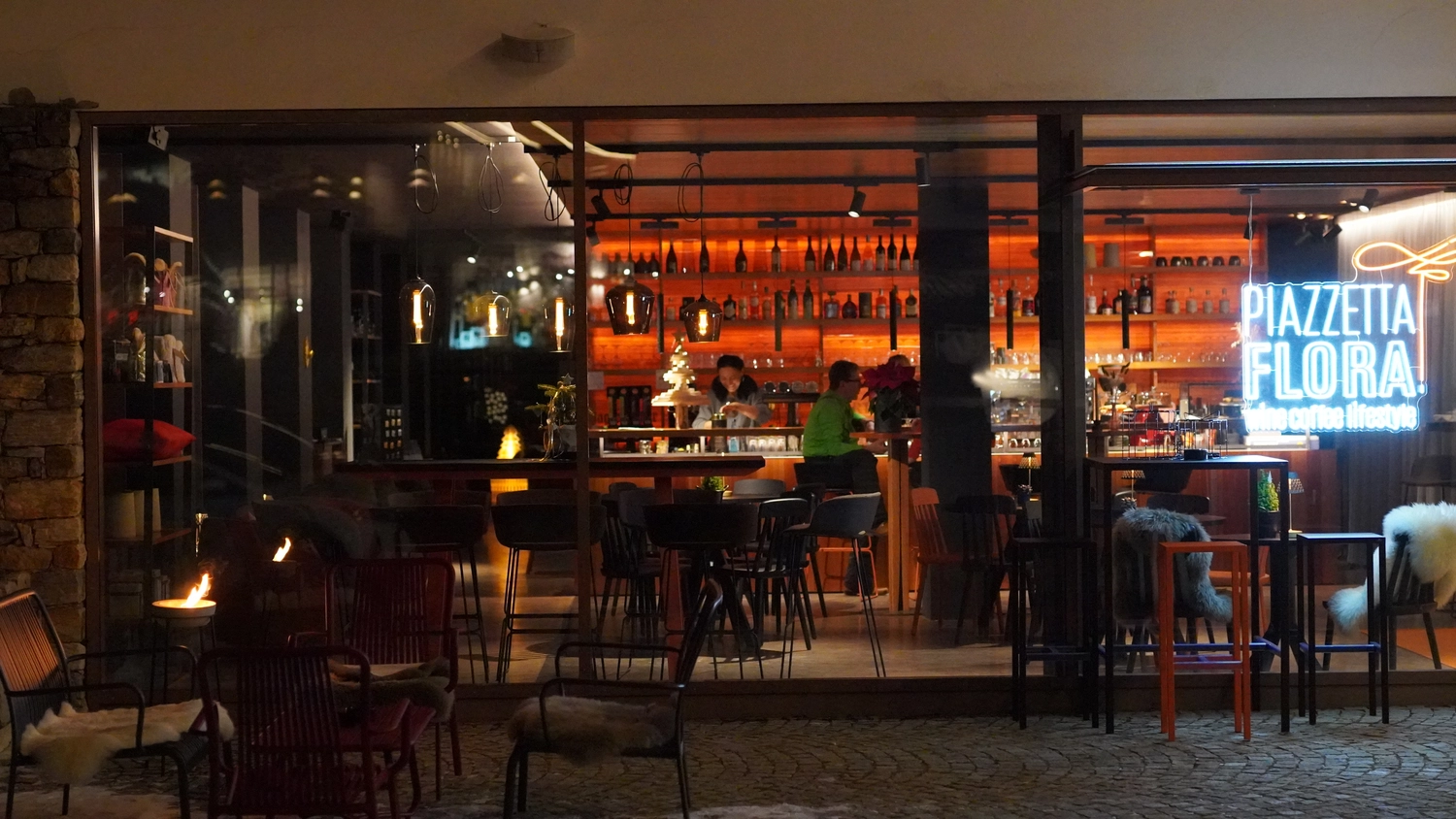 Sipho Studio - Drone visuel - Abendansicht vom Café "PIAZZETTA FLORA" mit warmen Lichtern, Bar und gemütlichen Außenplätzen.