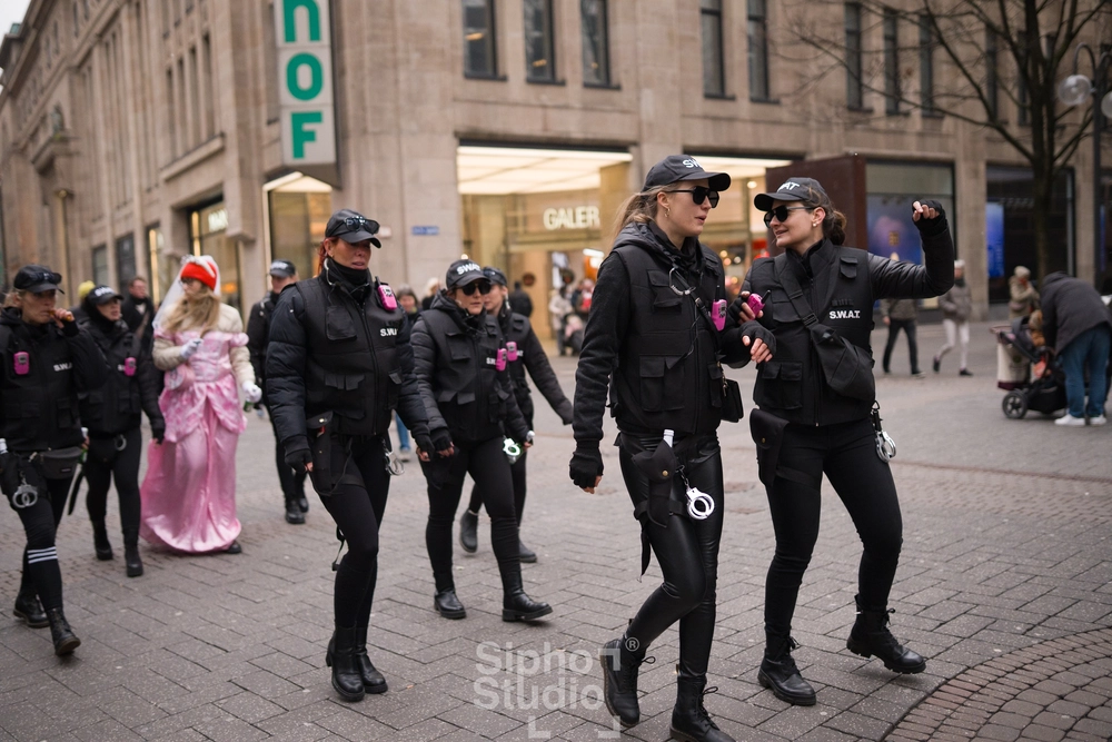 Sipho Studio - Drone visuel - Gruppe Frauen in schwarzen taktischen Outfits und Caps läuft lachend durch die Innenstadt.