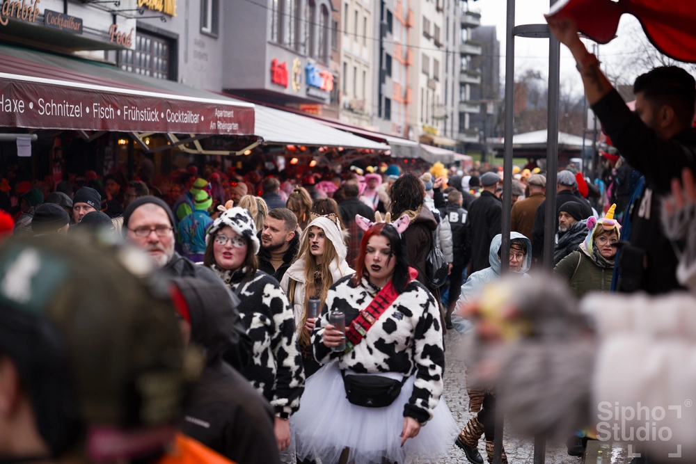 Sipho Studio - Drone visuel - Frauen im Kuh-Kostüm mit schwarzen Punkten und Tüllröcken beim Köln Karneval 2025 auf einem vollen Stadtplatz.