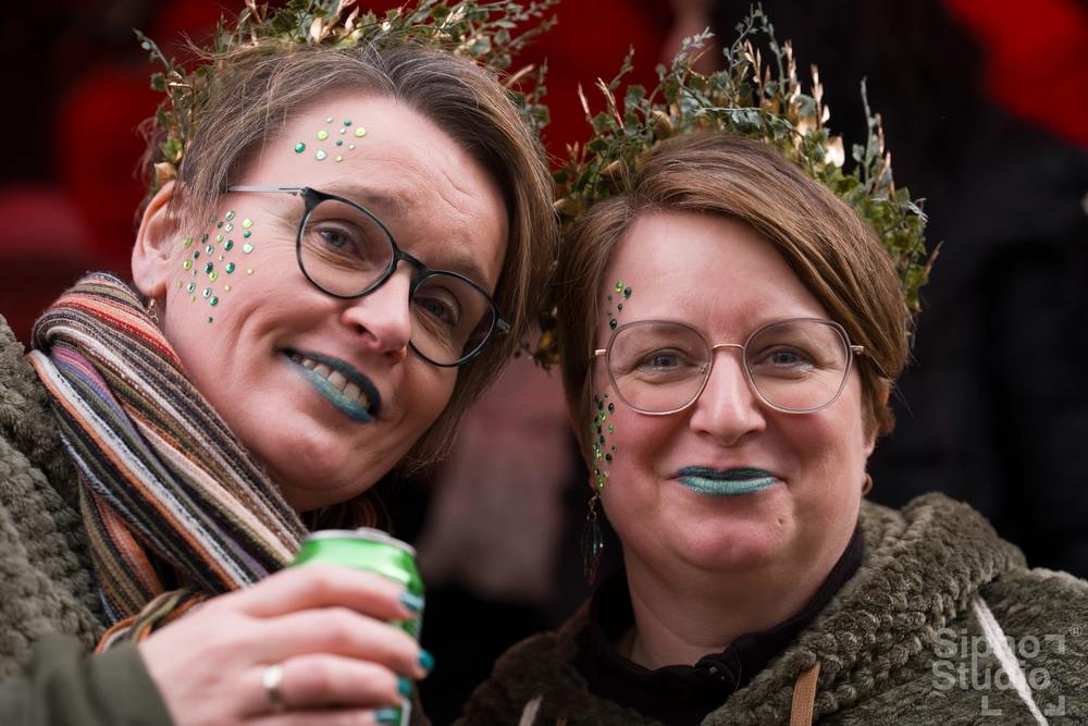 Sipho Studio - Drone visuel - Zwei Frauen mit Glitzer-Gesichtsbemalung und grünen Kränzen beim Köln Karneval 2025, lächeln in die Kamera.