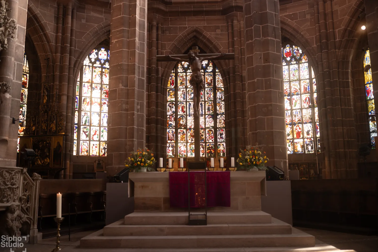 Sipho Studio - Drone visuel - Kircheninneres mit großem Kruzifix vor buntem Buntglasfenster und Altar mit Kerzen.