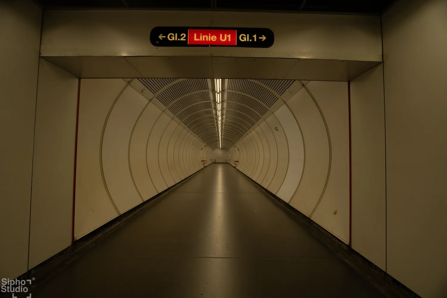 Sipho Studio - Drone visuel - Langer, heller U-Bahn-Tunnel mit runden Wänden und Schild für die Linien U1, GL1 und GL2.
