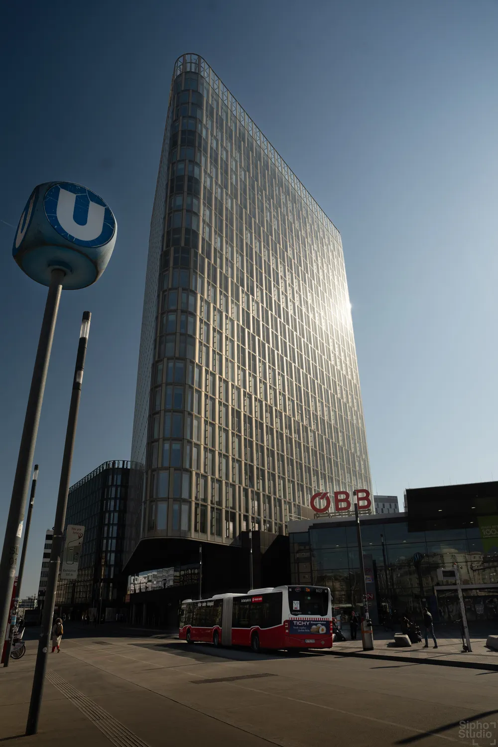 Sipho Studio - Drone visuel - Modernes Glas-Hochhaus mit ÖBB-Schriftzug neben einem blauen U-Bahn-Schild im Sonnenlicht.